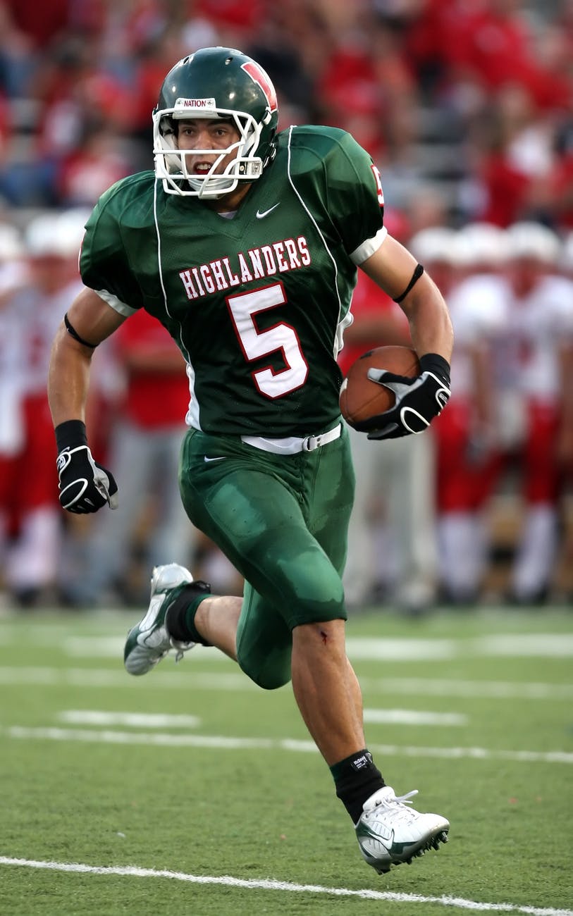 man wearing green american football jersey holding the ball while running on the field
