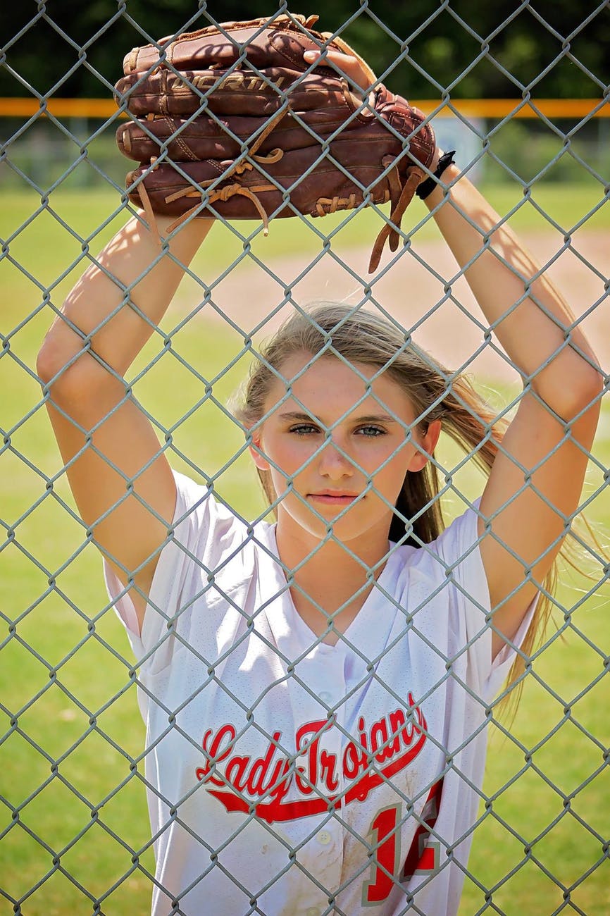 woman in white crew neck t shirt with baseball mitt in front of fence