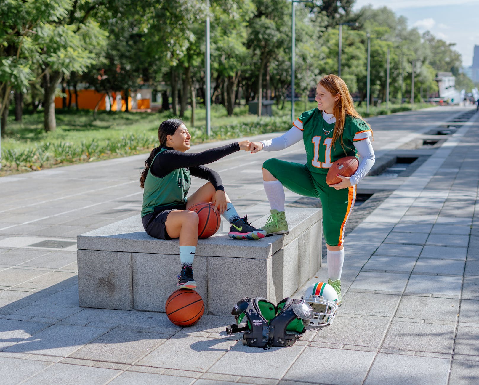 girl in basketball clothing and girl in american football clothing fist bumping